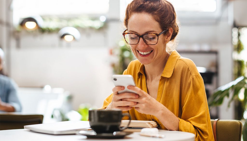 Woman with glasses sitting in cafe scrolling on a mobile phone